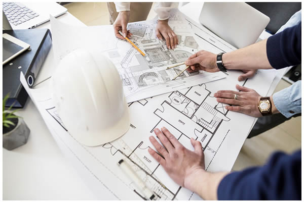 Photo of a hard hat sitting on top of a stack of blueprints on a table.