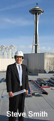 Photo of Steve Smith in construction hat on top of a building with space needle in the background.